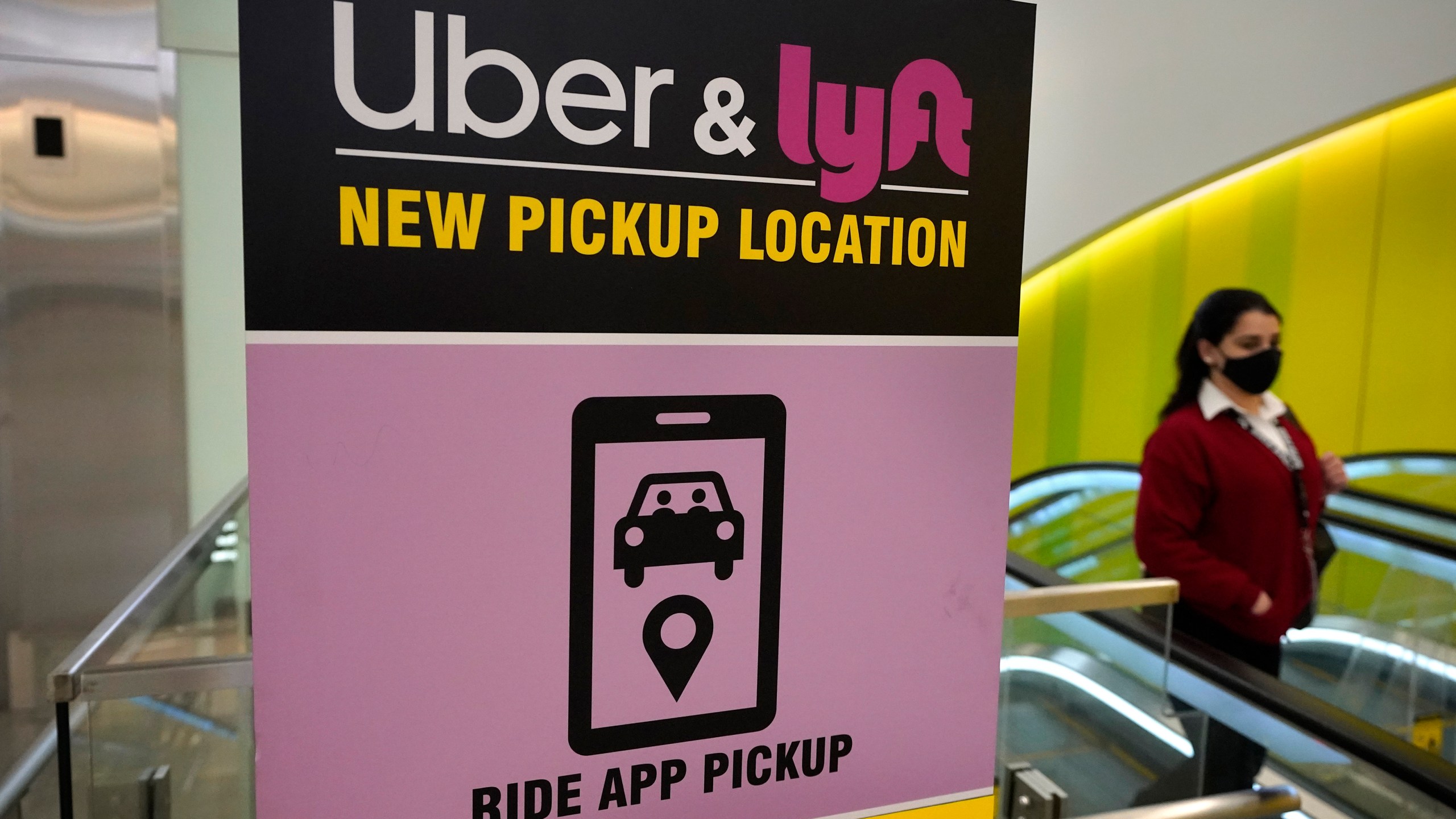 In this Feb. 9, 2021 photo, a passer-by walks past a sign offering directions to an Uber and Lyft ride pickup location at Logan International Airport in Boston. (Steven Senne/Associated Press)