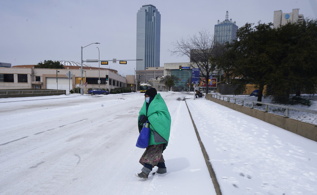 In this Feb. 16, 2021, file photo, a woman wrapped in a blanket crosses the street near downtown Dallas. As temperatures plunged and snow and ice whipped the state, much of Texas' power grid collapsed, followed by its water systems. Tens of millions huddled in frigid homes that slowly grew colder or fled for safety. (AP Photo/LM Otero, File)