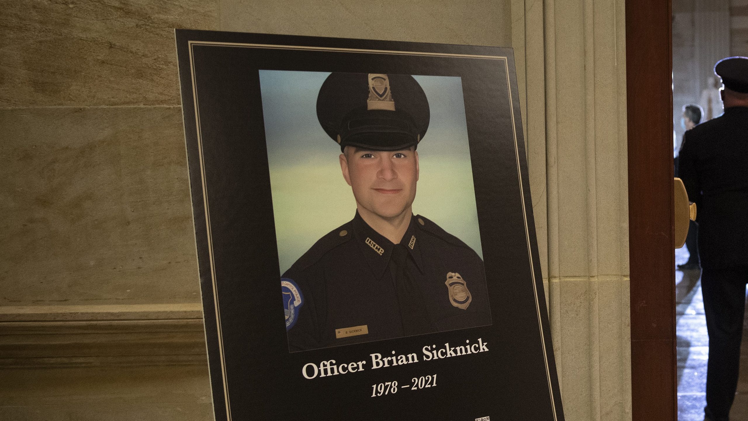 In this Feb. 2, 2021, file photo a placard is displayed with an image of the late U.S. Capitol Police officer Brian Sicknick on it as people wait for an urn with his cremated remains to be carried into the U.S. Capitol to lie in honor in the Capitol Rotunda in Washington. (Brendan Smialowski/Pool via AP, File)