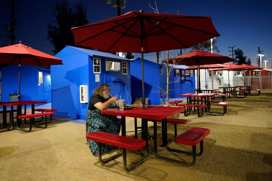 A resident eats in front of a row of tiny homes for the homeless on Feb. 25, 2021, in North Hollywood. (AP Photo/Marcio Jose Sanchez)