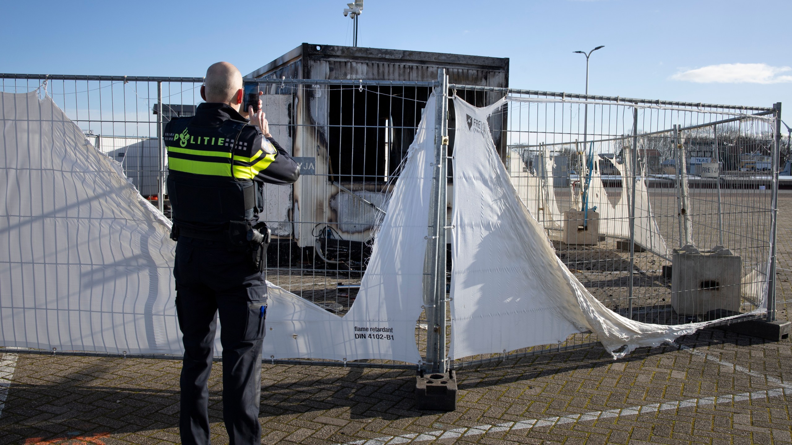 A police officer takes pictures of a burned-out coronavirus testing facility in the fishing village of Urk in the Netherlands on Jan. 24, 2021, after it was set on fire the night before by rioting youths protesting on the first night of a nationwide curfew. (Peter Dejong / Associated Press)