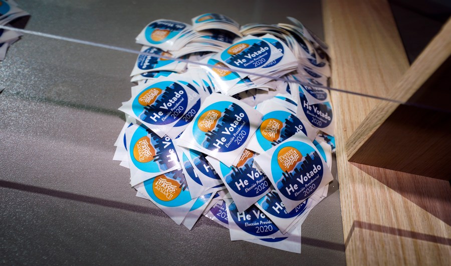 In this Oct. 30, 2020, file photo stickers printed in Spanish sit on the desk of an election judge to be distributed to voters after they cast their ballots in the atrium of Ball Arena, the home of the NBA's Denver Nuggets and the NHL's Colorado Avalanche in Denver. (AP Photo/David Zalubowski, File)