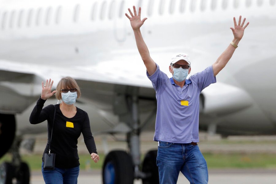 In this March 10, 2020, file photo, passengers from the Grand Princess, a cruise ship carrying multiple people who have tested positive for COVID-19, gesture toward reporters while walking on a tarmac before boarding a chartered plane in Oakland, Calif., on March 10, 2020. (AP Photo/Jeff Chiu, File)