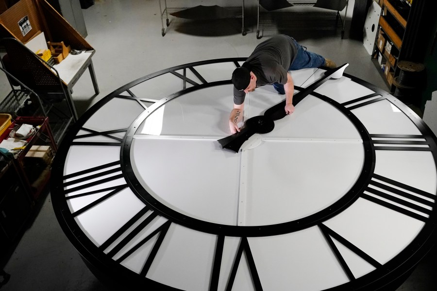 Electric Time technician Dan LaMoore puts a clock hand onto a 1000-lb., 12-foot diameter clock constructed for a resort in Vietnam, Tuesday, March 9, 2021, in Medfield, Mass. Daylight saving time begins at 2 a.m. local time Sunday, March 14, 2021, when clocks are set ahead one hour. (AP Photo/Elise Amendola)