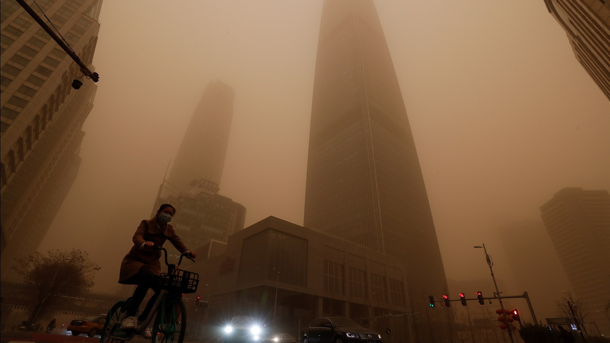 A cyclist and motorists move past office buildings amid a sandstorm during the morning rush hour in the central business district in Beijing, Monday, March 15, 2021. (AP Photo/Andy Wong)