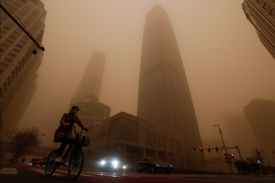 A cyclist and motorists move past office buildings amid a sandstorm during the morning rush hour in the central business district in Beijing, Monday, March 15, 2021. (AP Photo/Andy Wong)