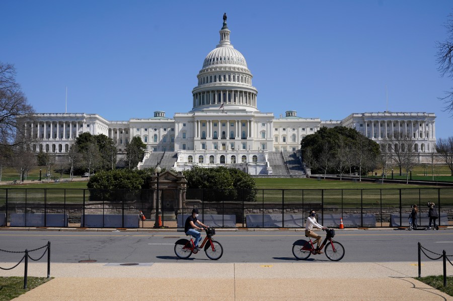 Bicyclists ride past an inner perimeter of security fencing on Capitol Hill in Washington, Sunday, March 21, 2021, after portions of an outer perimeter of fencing were removed overnight to allow public access. (AP Photo/Patrick Semansky)