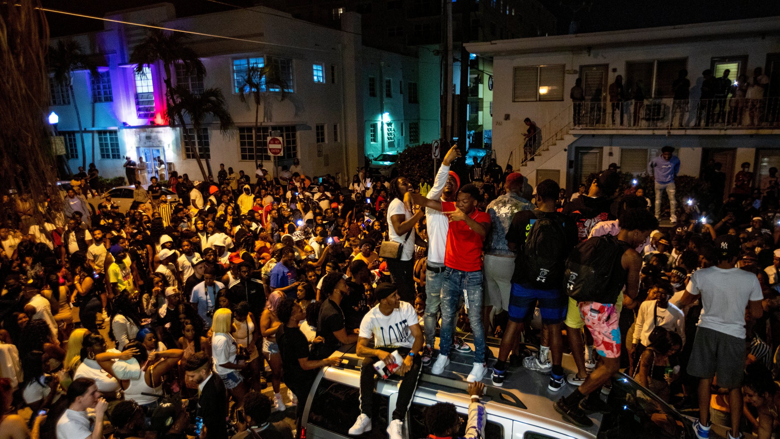 Crowds defiantly gather in the street while a speaker blasts music an hour past curfew in Miami Beach, Fla., on Sunday, March 21, 2021. An 8 p.m. curfew has been extended in Miami Beach after law enforcement worked to contain unruly crowds of spring break tourists. (Daniel A. Varela/Miami Herald via AP)