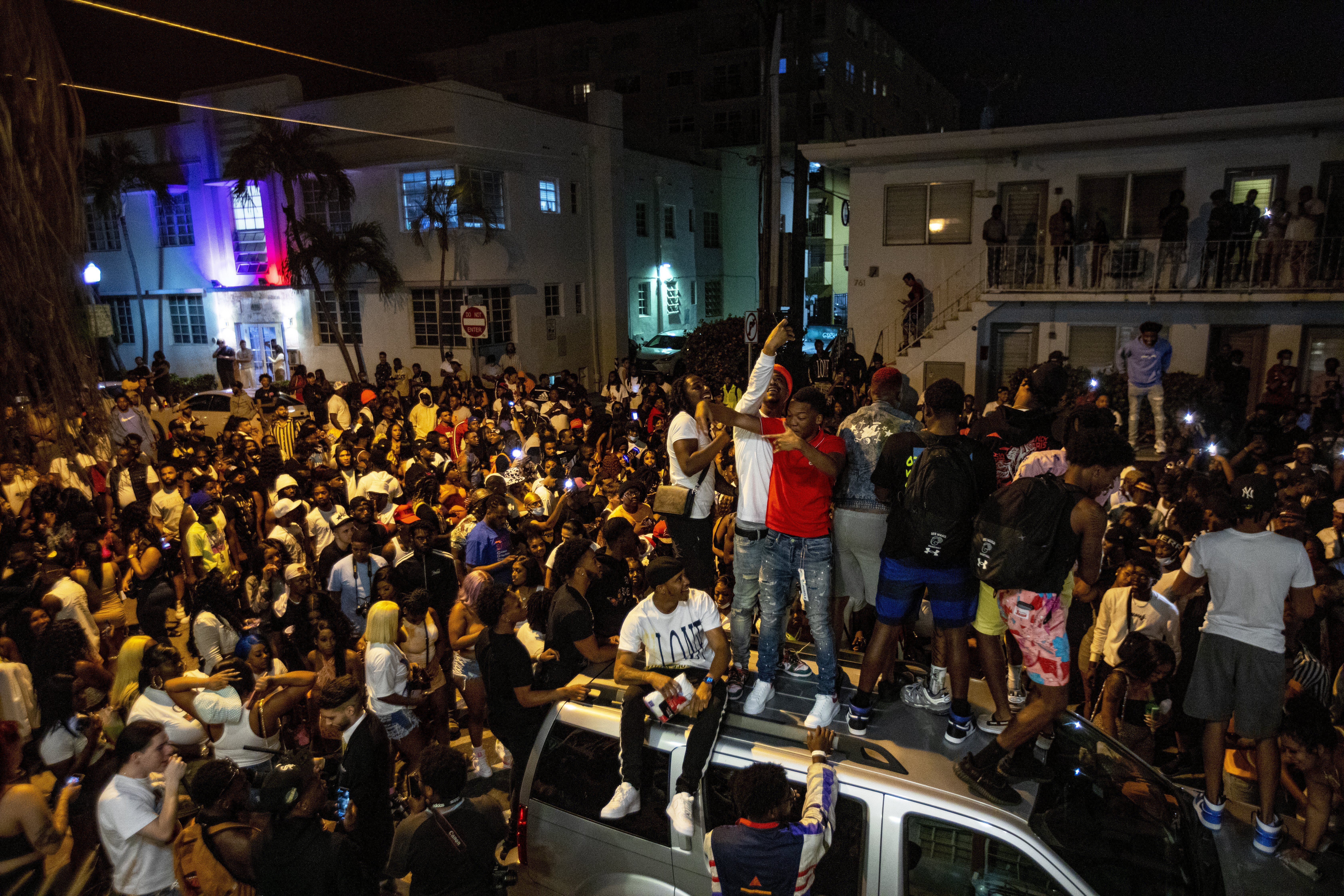 Crowds defiantly gather in the street while a speaker blasts music an hour past curfew in Miami Beach, Fla., on Sunday, March 21, 2021. An 8 p.m. curfew has been extended in Miami Beach after law enforcement worked to contain unruly crowds of spring break tourists. (Daniel A. Varela/Miami Herald via AP)