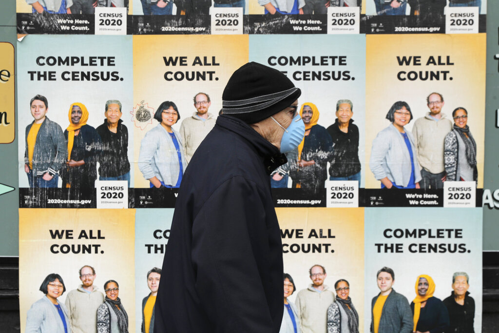 In this April 1, 2020, file photo, a man wearing a mask walks past posters encouraging participation in the 2020 Census in Seattle's Capitol Hill neighborhood. (AP Photo/Ted S. Warren, File)