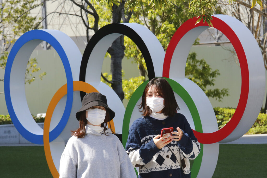 In this March 17, 2021, file photo, people walk past the Olympic rings in Tokyo. The Tokyo Olympics open in under four months, and the torch relay has begun to crisscross Japan with 10,000 runners. (AP Photo/Koji Sasahara)