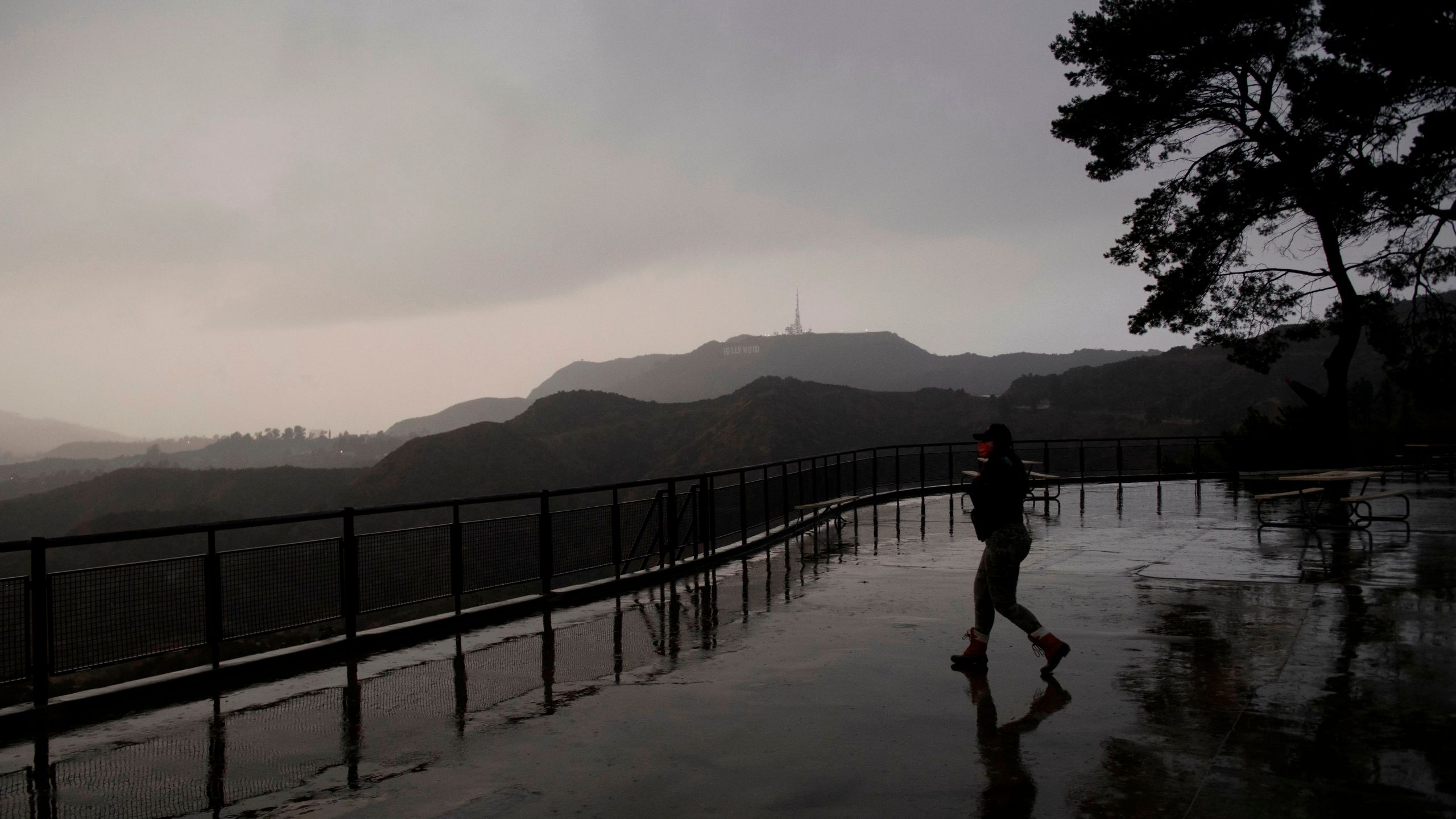 A person wears a face mask while walking to take pictures from a viewing area overlooking the Hollywood sign shrouded by clouds during heavy rains as seen from the Griffith Observatory on Dec. 28, 2020, in Los Angeles, California. (Patrick T. Fallon/AFP via Getty Images)