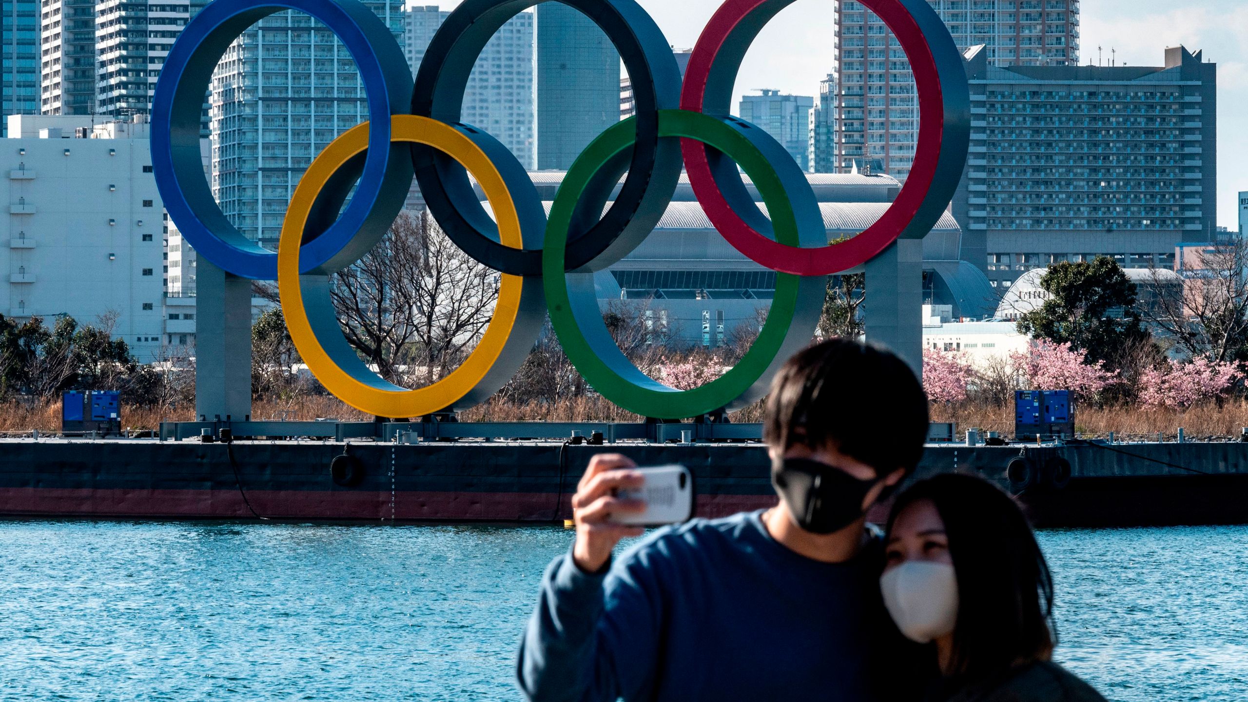 A couple pose for photos in front of the Olympic rings on display at the Odaiba waterfront in Tokyo on Feb. 24, 2021. (PHILIP FONG/AFP via Getty Images)