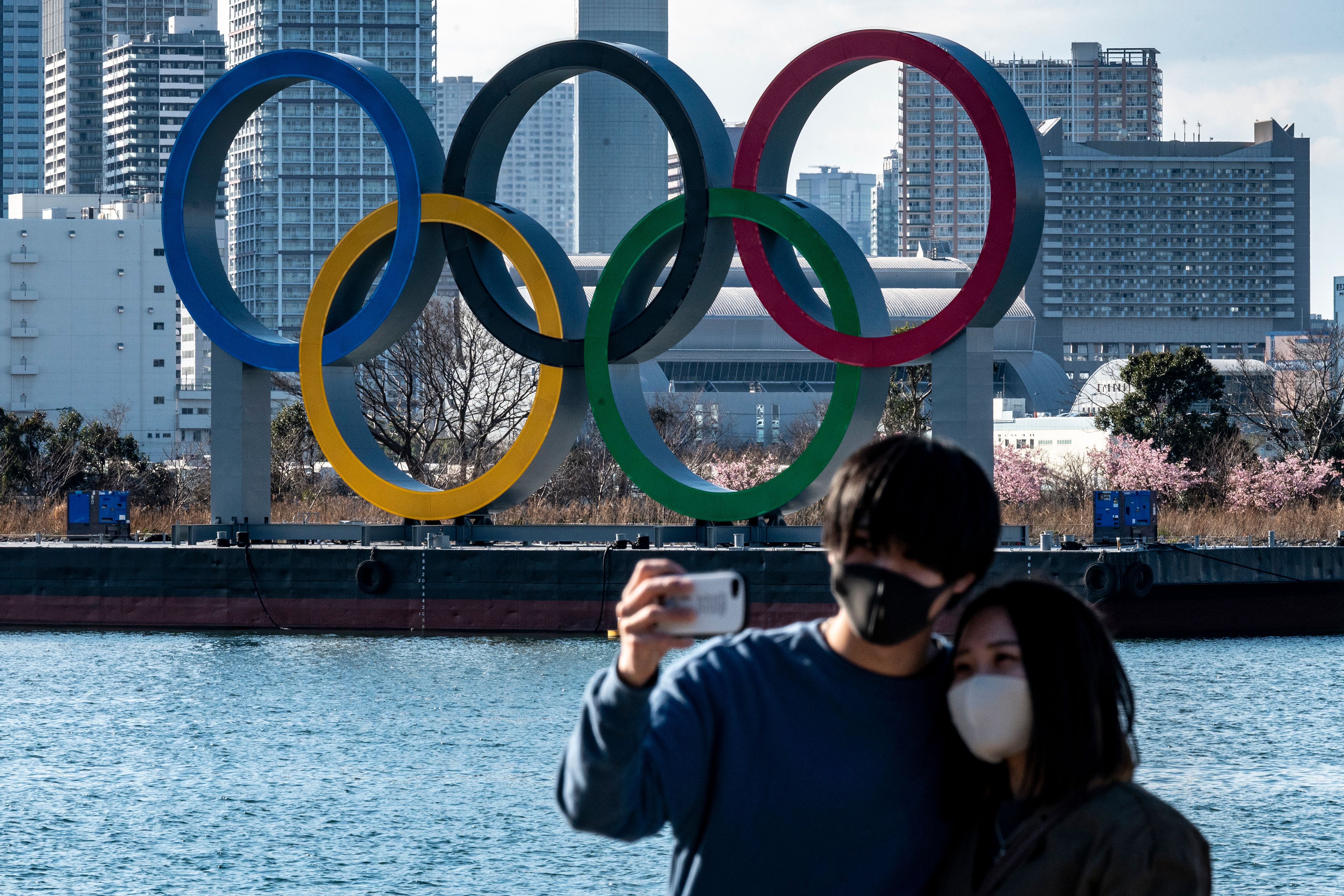 A couple pose for photos in front of the Olympic rings on display at the Odaiba waterfront in Tokyo on Feb. 24, 2021. (PHILIP FONG/AFP via Getty Images)