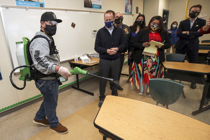 Plant manager Sergio Ruiz, left, demonstrates the use of a electrostatic sprayer to disinfect a classroom at Panorama High School on March 10, 2021, as L.A. Unified Supt. Austin Beutner and UTLA President Cecily Myart-Cruz watch.(Irfan Khan / Los Angeles Times)