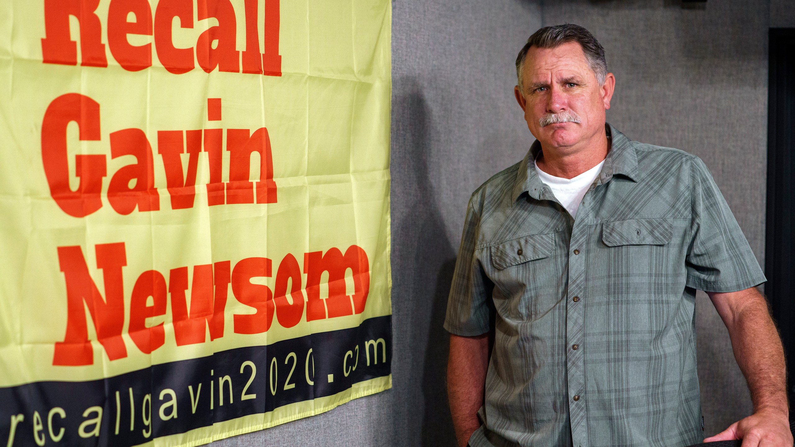 Orrin Heatlie, the main organizer for the recall of California Gov. Newsom campaign, poses with a banner before recording a radio program at the KABC radio station studio in Culver City, March 27, 2021. (AP Photo/Damian Dovarganes)