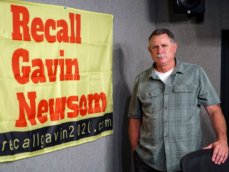 Orrin Heatlie, the main organizer for the recall of California Gov. Newsom campaign, poses with a banner before recording a radio program at the KABC radio station studio in Culver City, March 27, 2021. (AP Photo/Damian Dovarganes)