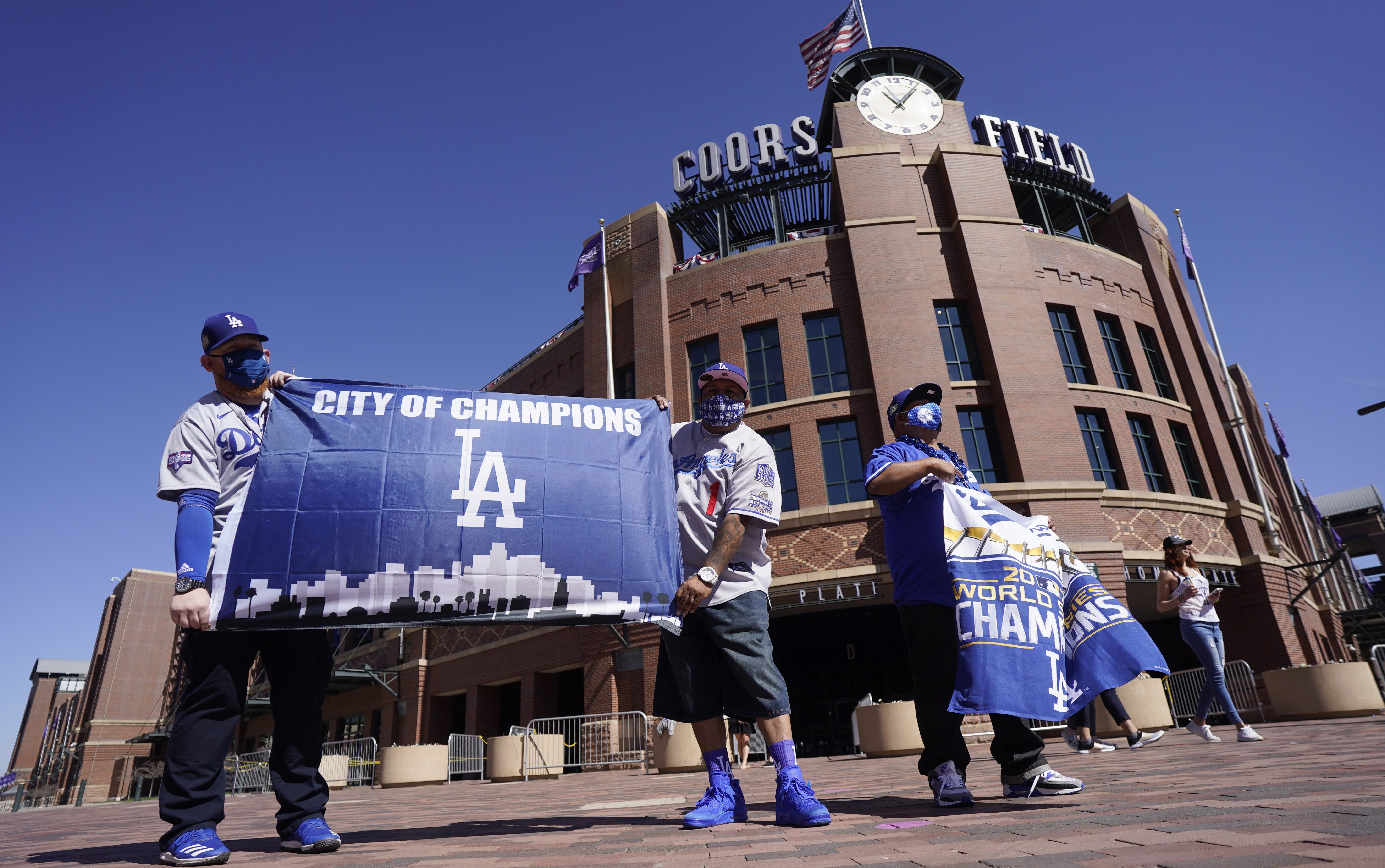 Los Angeles Dodgers fans Oliver Olson, left, of San Diego, Juan Campo and Rudy Soto, both of Los Angeles, hold up flags outside the main entrance to Coors Field in Denver as fans return for the first inning of a baseball game between the Dodgers and Colorado Rockies on April 1, 2021. (David Zalubowski / Associated Press)