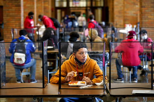 In this March 31, 2021, file photo, freshman Hugo Bautista eats lunch separated from classmates by plastic dividers at Wyandotte County High School in Kansas City, Kan., on the first day of in-person learning. With a massive infusion of federal aid coming their way, schools across the U.S. are weighing how to use the windfall to ease the harm of the pandemic — and to tackle problems that existed long before the coronavirus. (AP Photo/Charlie Riedel, File)