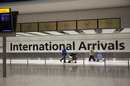 In this Tuesday, Jan. 26, 2021 file photo, arriving passengers walk past a sign in the arrivals area at Heathrow Airport in London, during England's third national lockdown since the coronavirus outbreak began. (AP Photo/Matt Dunham, File)