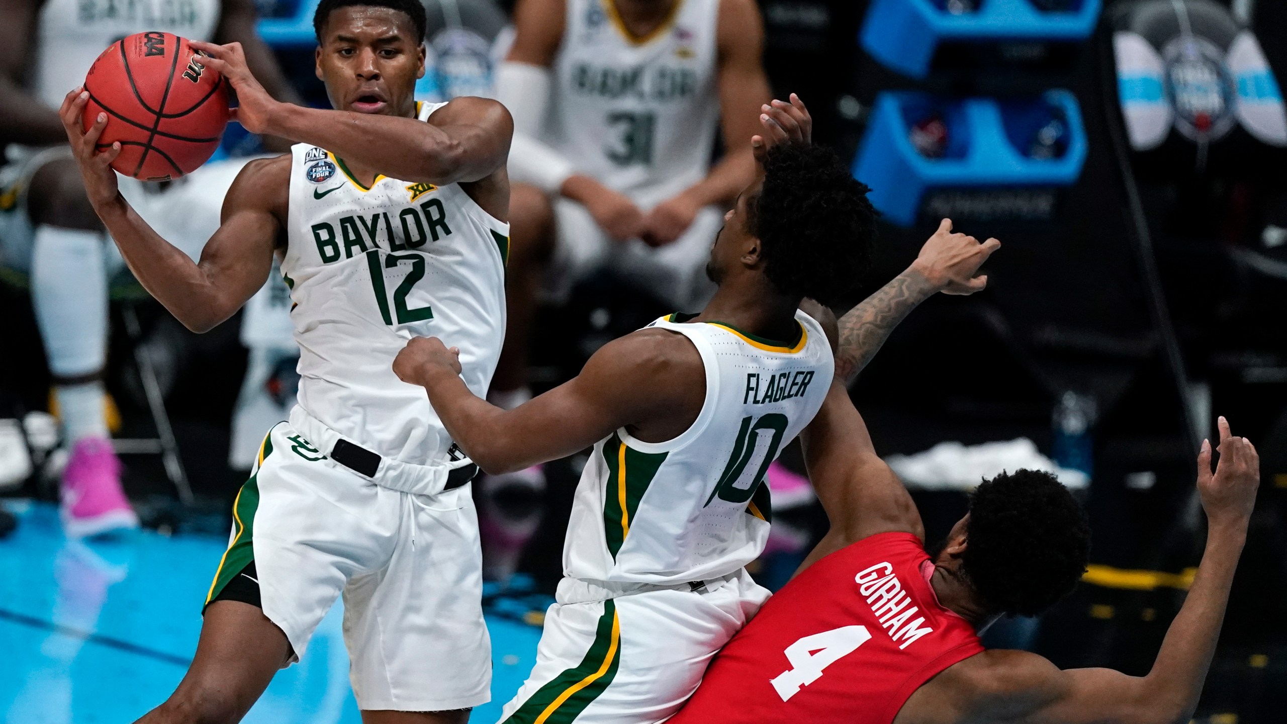 Baylor guard Jared Butler (12) passes over teammate guard Adam Flagler (10) and Houston forward Justin Gorham (4) during the first half of a men's Final Four NCAA college basketball tournament semifinal game, Saturday, April 3, 2021, at Lucas Oil Stadium in Indianapolis. (AP Photo/Michael Conroy)