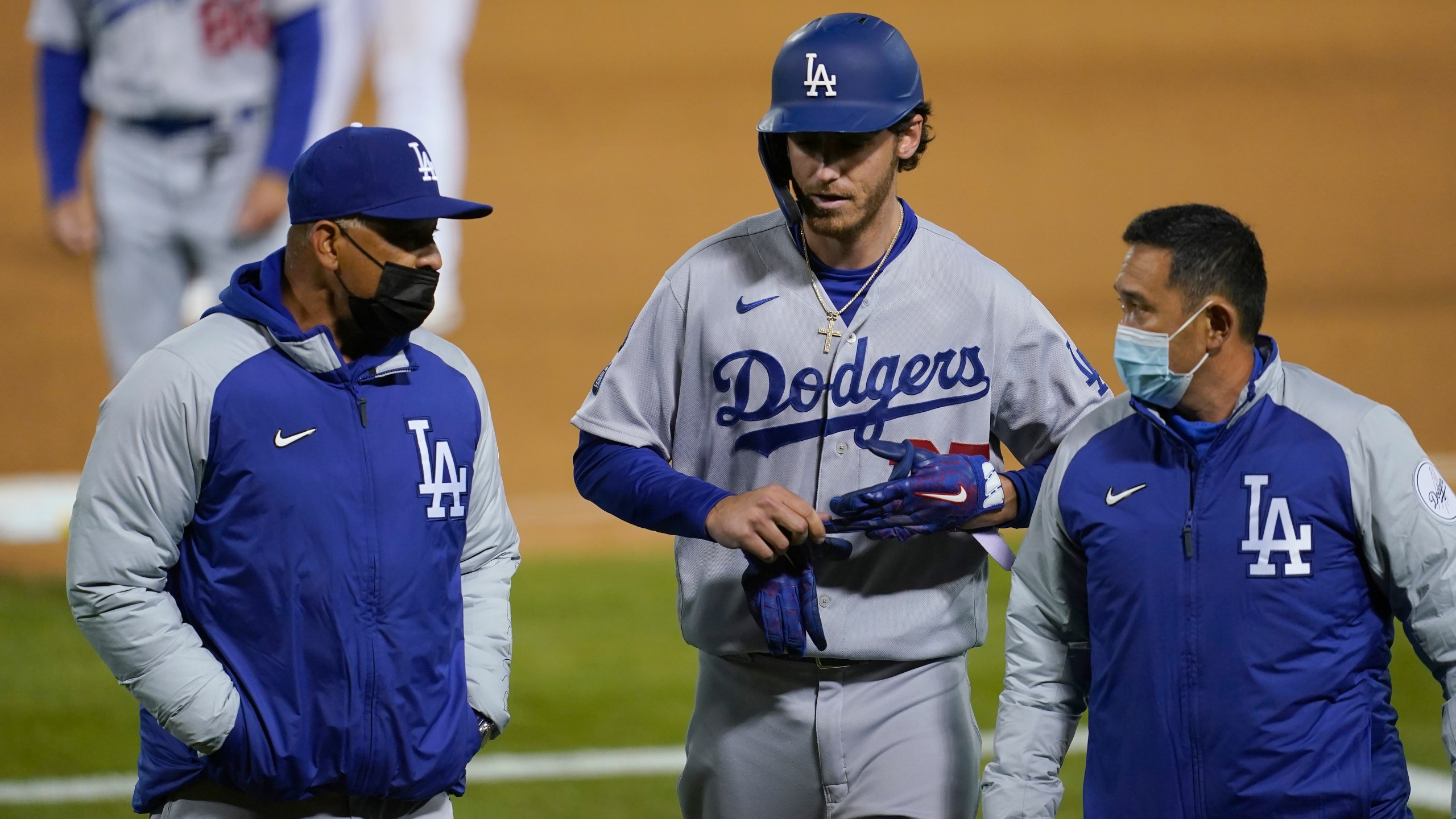 Los Angeles Dodgers' Cody Bellinger, center, walks off the field as he leaves the game with manager Dave Roberts, left, and a trainer during the ninth inning of a baseball game against the Oakland Athletics in Oakland on April 5, 2021. (Jeff Chiu / Associated Press)