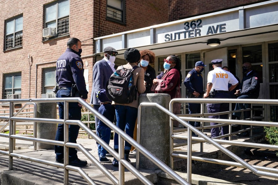 Police officers and community leaders stand outside the building where a man shot the mother of his child and two of her daughters dead before turning the gun on himself, Tuesday, April 6, 2021, in the Brownsville neighborhood of the Brooklyn borough of New York. (AP Photo/Mary Altaffer)