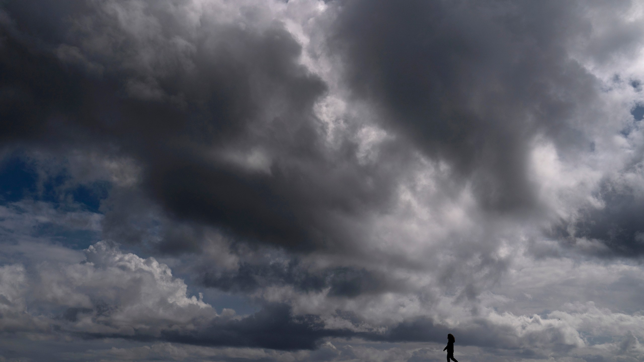 A woman strolls along the beach under rain clouds in Seal Beach on March 10, 2021. (Jae C. Hong / Associated Press)