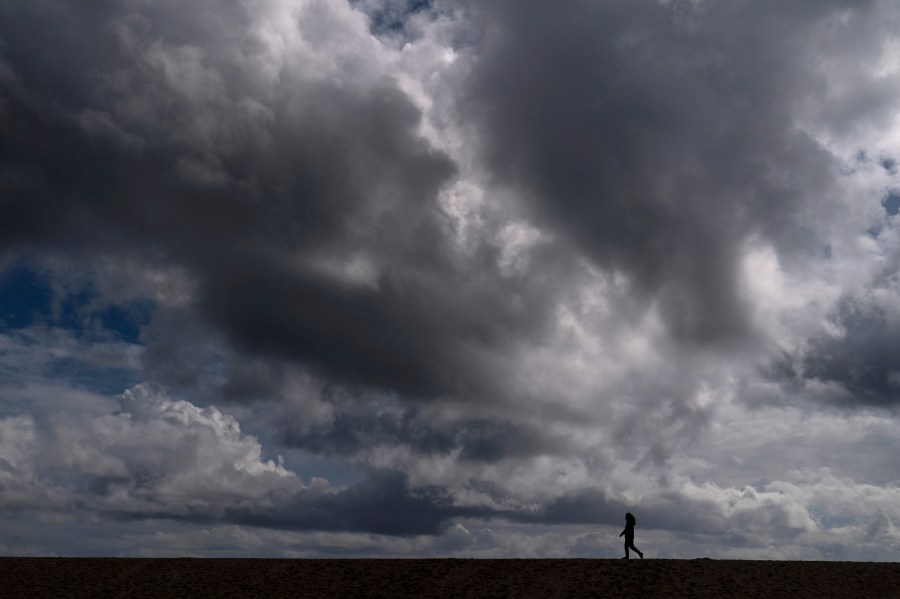 A woman strolls along the beach under rain clouds in Seal Beach on March 10, 2021. (Jae C. Hong / Associated Press)