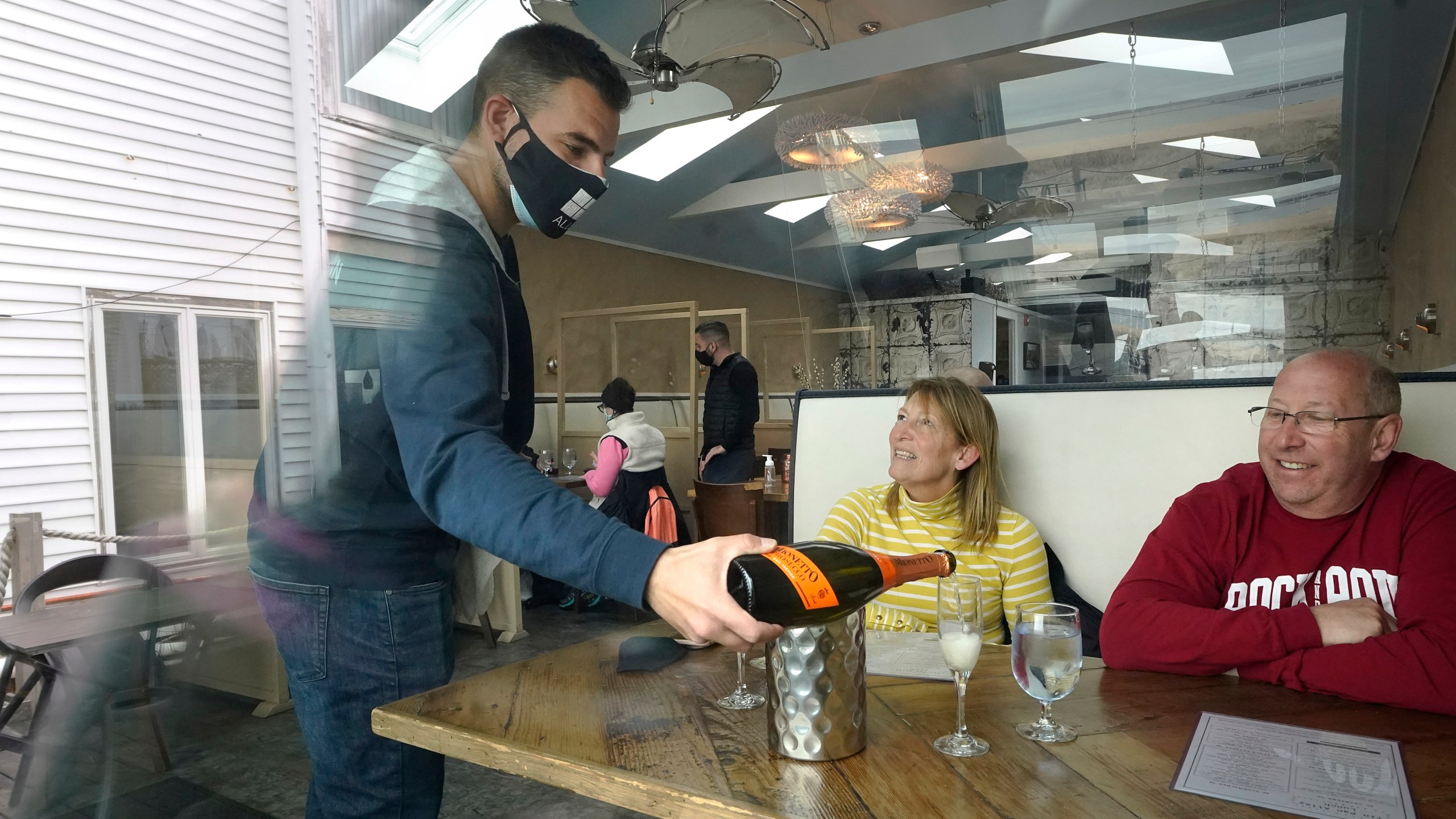 Bartender Denis Angelov, of Provincetown, Mass., left, serves sparking wine to Julie Skaller, left, and her husband David Skaller, right, both of Brewster, N.Y., at Tin Pan Alley restaurant, Tuesday, April 6, 2021, in Provincetown. (AP Photo/Steven Senne)