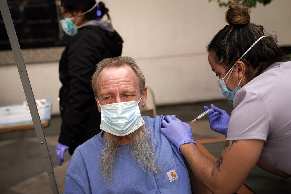 In this Feb. 3, 2021, file photo, EMT Rachel Bryant, right, administers a COVID-19 vaccine to a homeless man in the courtyard of the Midnight Mission in Los Angeles. (AP Photo/Jae C. Hong)