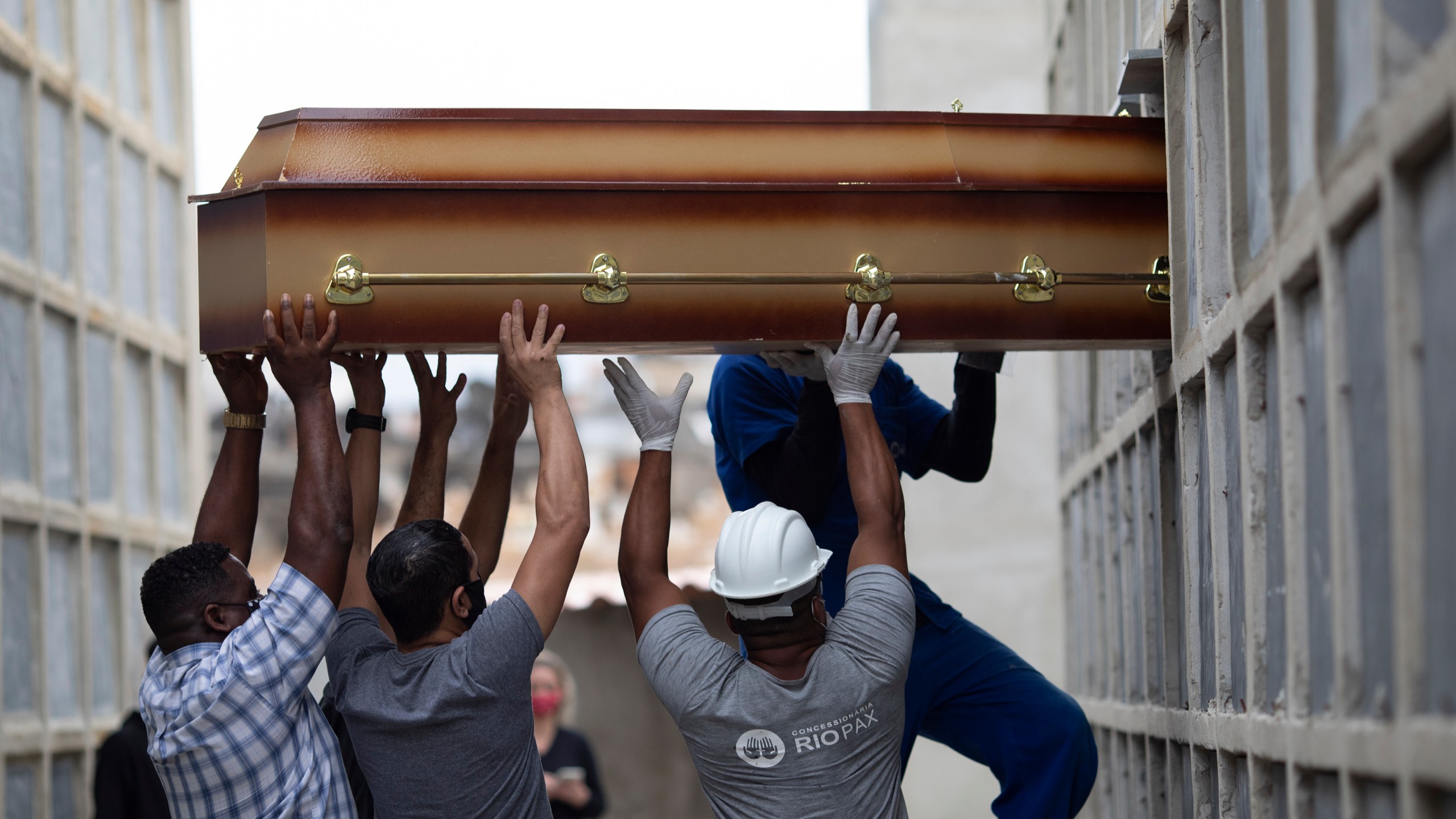 In this April 13, 2021, file photo, the remains of a woman who died from complications related to COVID-19 are placed into a niche by cemetery workers and relatives at the Inahuma cemetery in Rio de Janeiro, Brazil. (AP Photo/Silvia Izquierdo, File)