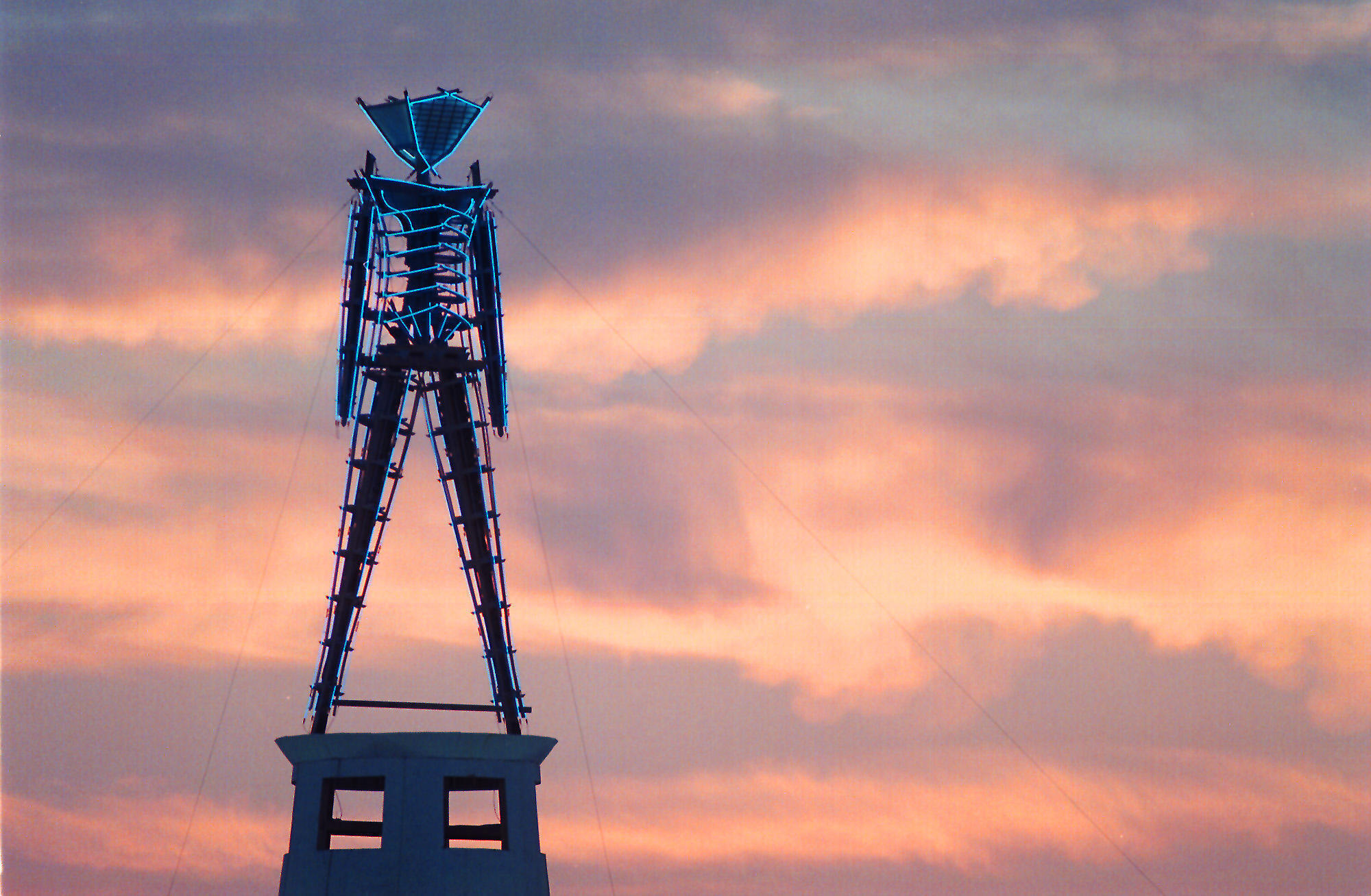 The sun rises behind a wood and neon statue, the center piece of the annual Burning Man festival north of Gerlach, Nev., on Aug. 26, 2002. (Debra Reid / Associated Press)