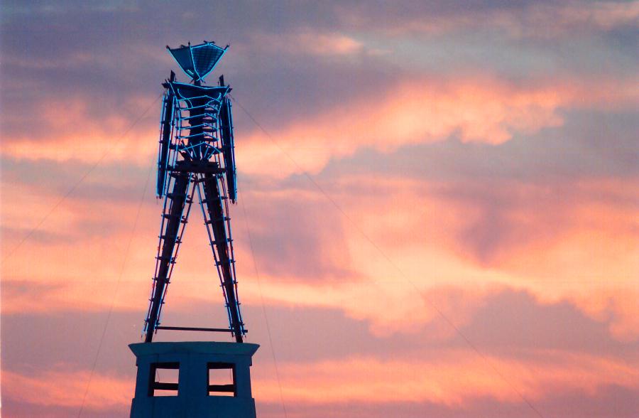 The sun rises behind a wood and neon statue, the center piece of the annual Burning Man festival north of Gerlach, Nev., on Aug. 26, 2002. (Debra Reid / Associated Press)