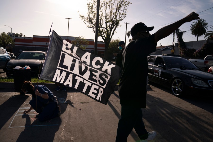 A person with a Black Lives Matter flag writes a message on a sidewalk at the intersection of Florence and Normandie Avenues in Los Angeles, on April 20, 2021, after a guilty verdict was announced at the trial of former Minneapolis police Officer Derek Chauvin for the 2020 death of George Floyd. (AP Photo/Jae C. Hong)