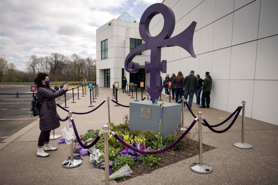 A fan takes a photo of a memorial on April 21, 2021 as others line up to go into Paisley Park in Chanhassen, Minn., on the fifth anniversary of Prince's death. (Stacy Bengs/Associated Press)