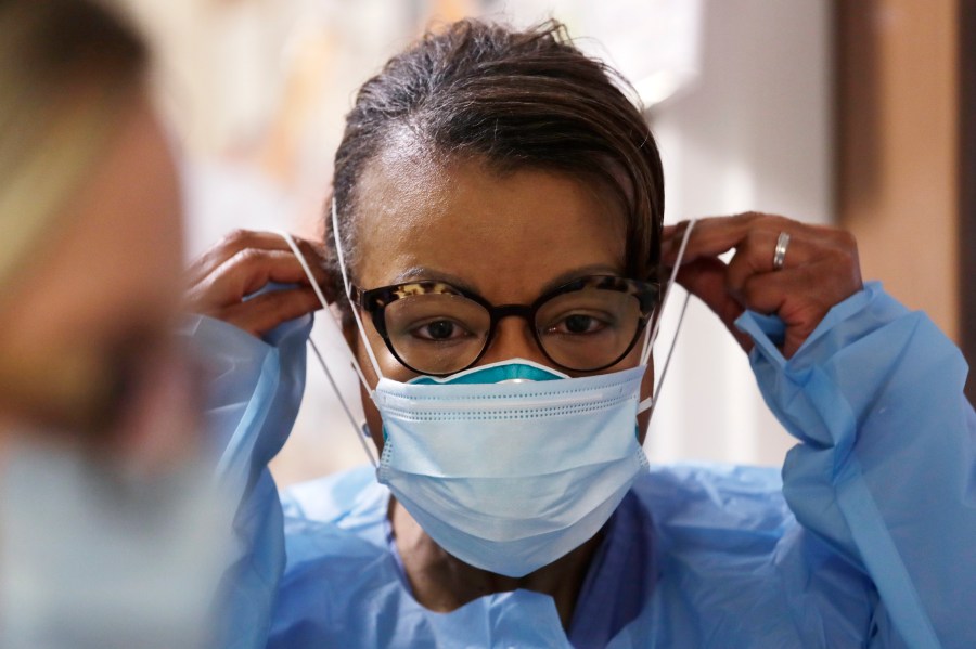 In this Friday, May 8, 2020 file photo, a respiratory therapist pulls on a second mask over her N95 mask before adding a face shield as she gets ready to go into a patient's room in the COVID-19 Intensive Care Unit at a hospital in Seattle. (AP Photo/Elaine Thompson)