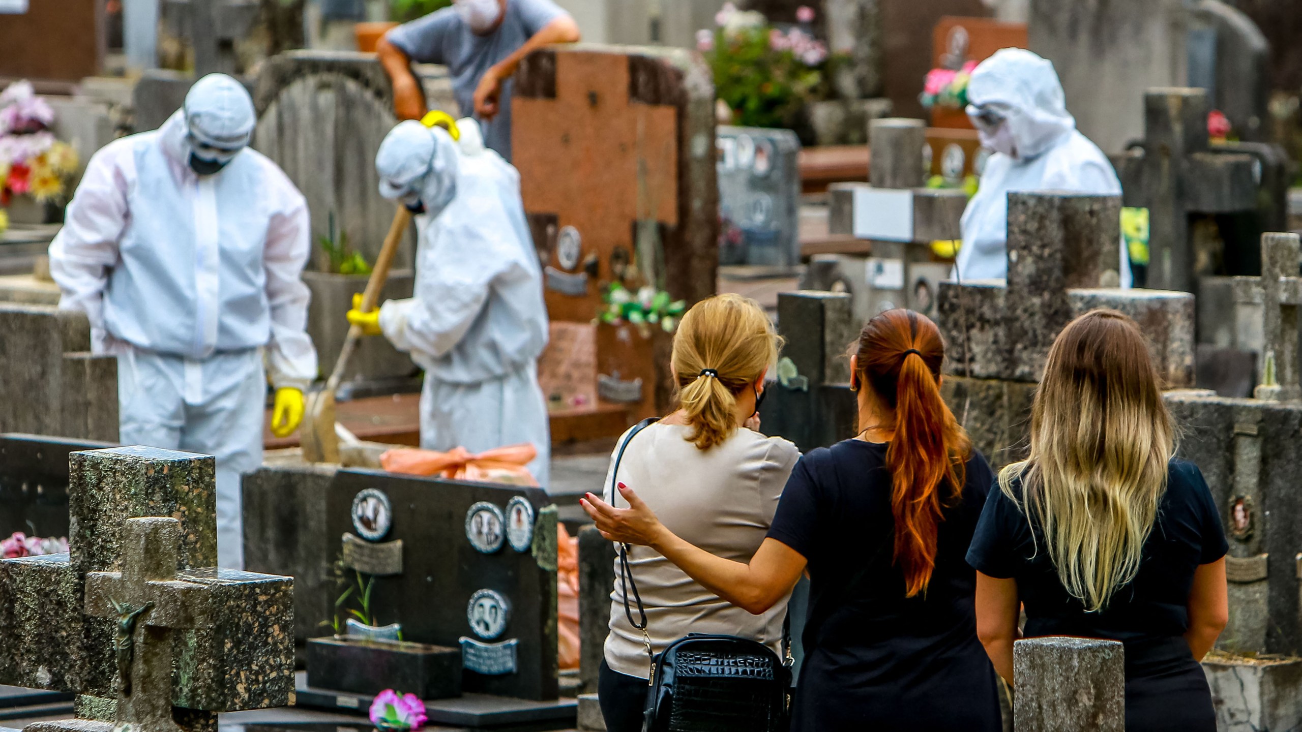 Relatives of a victim of COVID-19 watch as cemetery workers clean graves after a burial at the Sao Joao municipal cemetery in Porto Alegre, Brazil, on March 26, 2021. Brazil surpassed 100,000 new COVID-19 cases in one day that Thursday, adding another grim record in a country where the pandemic has killed more than 300,000 people. (SILVIO AVILA / AFP via Getty Images)