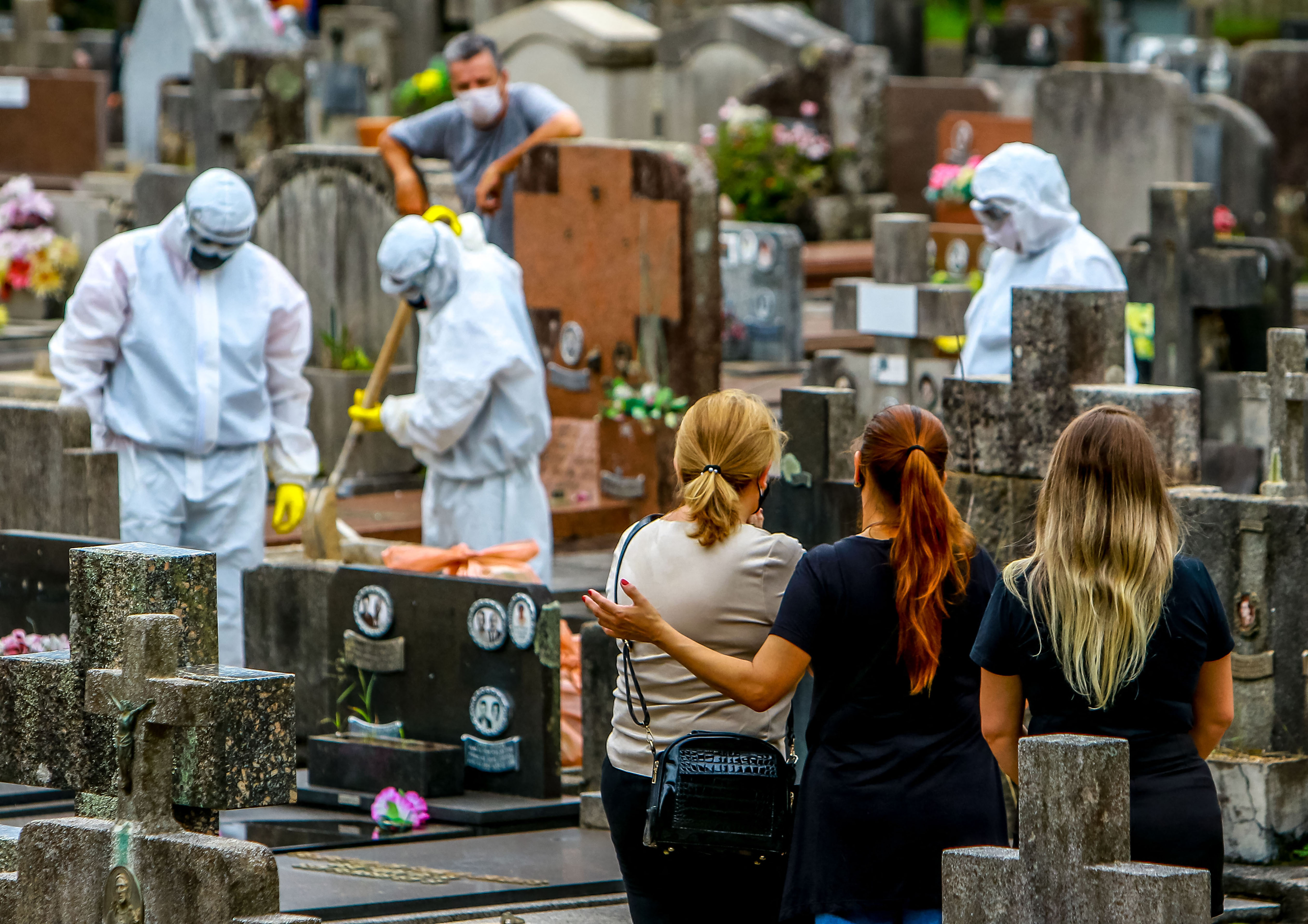 Relatives of a victim of COVID-19 watch as cemetery workers clean graves after a burial at the Sao Joao municipal cemetery in Porto Alegre, Brazil, on March 26, 2021. Brazil surpassed 100,000 new COVID-19 cases in one day that Thursday, adding another grim record in a country where the pandemic has killed more than 300,000 people. (SILVIO AVILA / AFP via Getty Images)