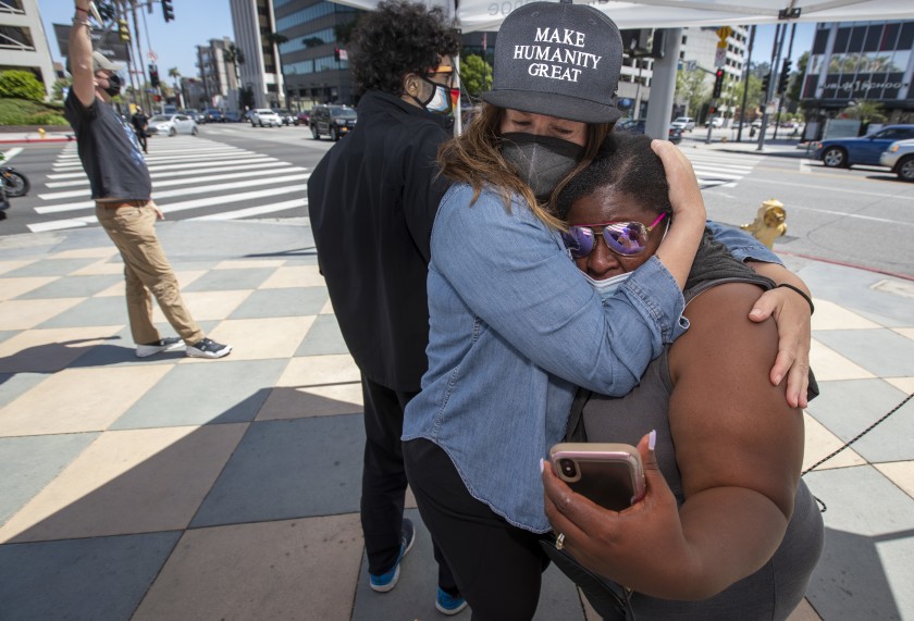 Katie Mau, left, embraces Latora Green in Sherman Oaks as the verdicts are read in the Derek Chauvin trial on April 20, 2021. Green has been standing in front of the Sherman Oaks Galleria on Ventura and Sepulveda boulevards for 325 straight days. (Brian van der Brug / Los Angeles Times)