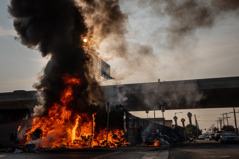 A homeless encampment burns at South Grand Avenue and West 54th Street, next to the 110 Freeway, in October 2020. (Jay L. Clendenin / Los Angeles Times)