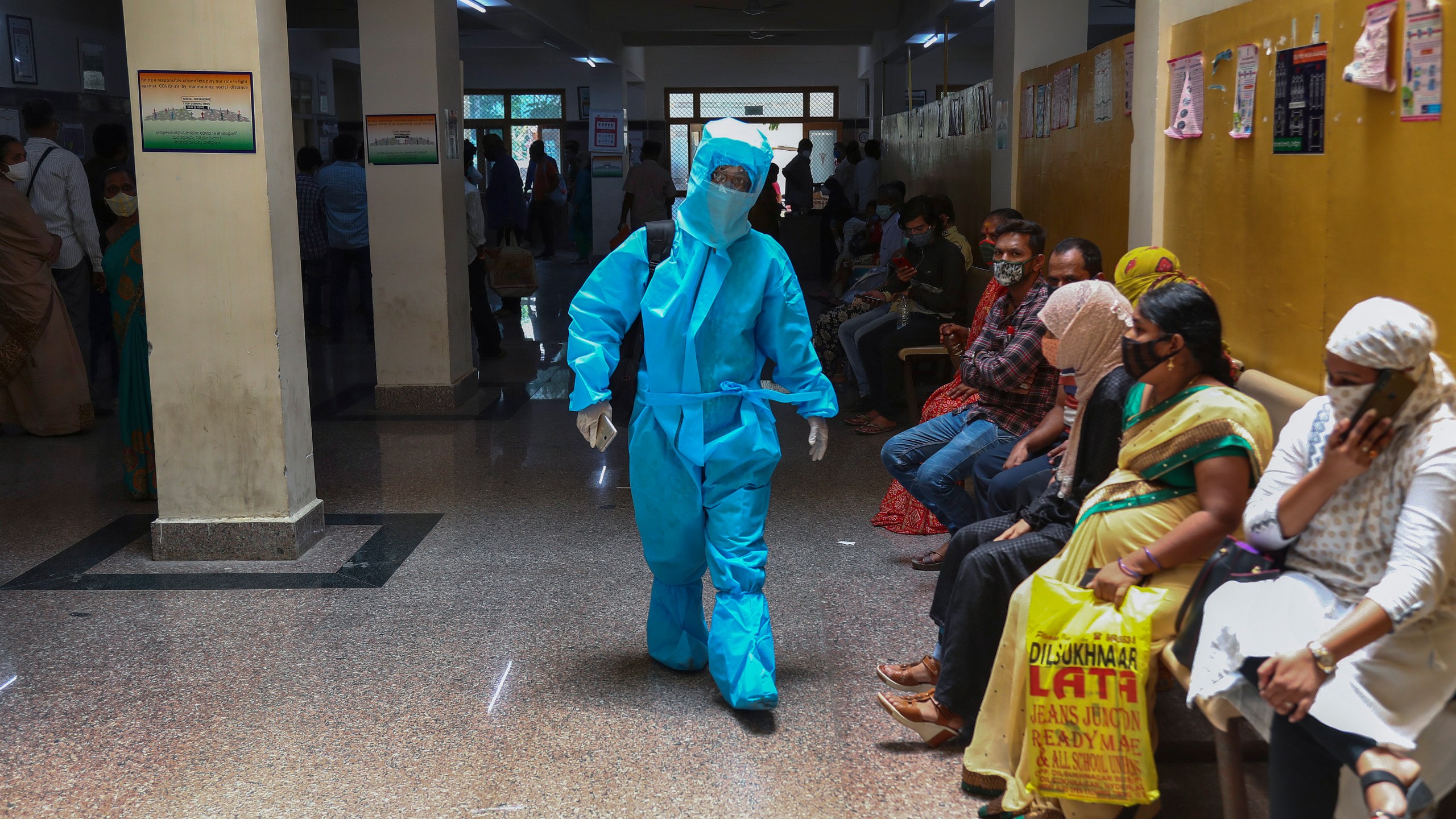 An Indian woman in personal protective suit walks towards a COVID-19 ward of a hospital as others waits for their test results in Hyderabad, India, Thursday, April 29, 2021. (AP Photo/Mahesh Kumar A.)