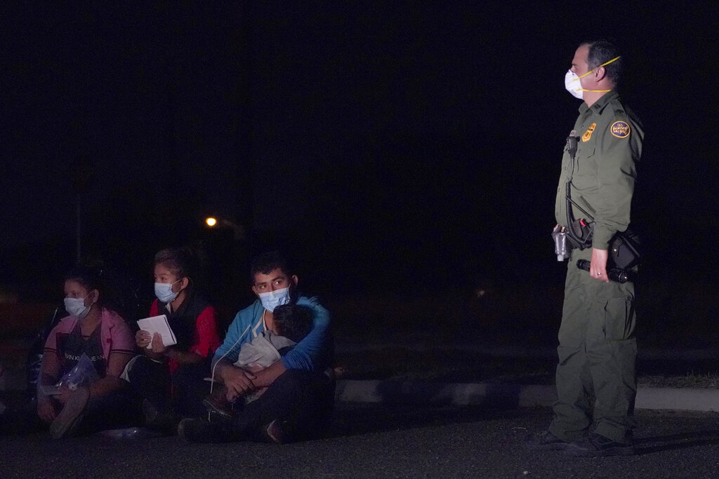 In this March 24, 2021 photo, a migrant man, center, holds a child as he looks at a U.S. Customs and Border Protection agent at an intake area after crossing the U.S.-Mexico border, early Wednesday, March 24, 2021, in Roma, Texas. (AP Photo/Julio Cortez)