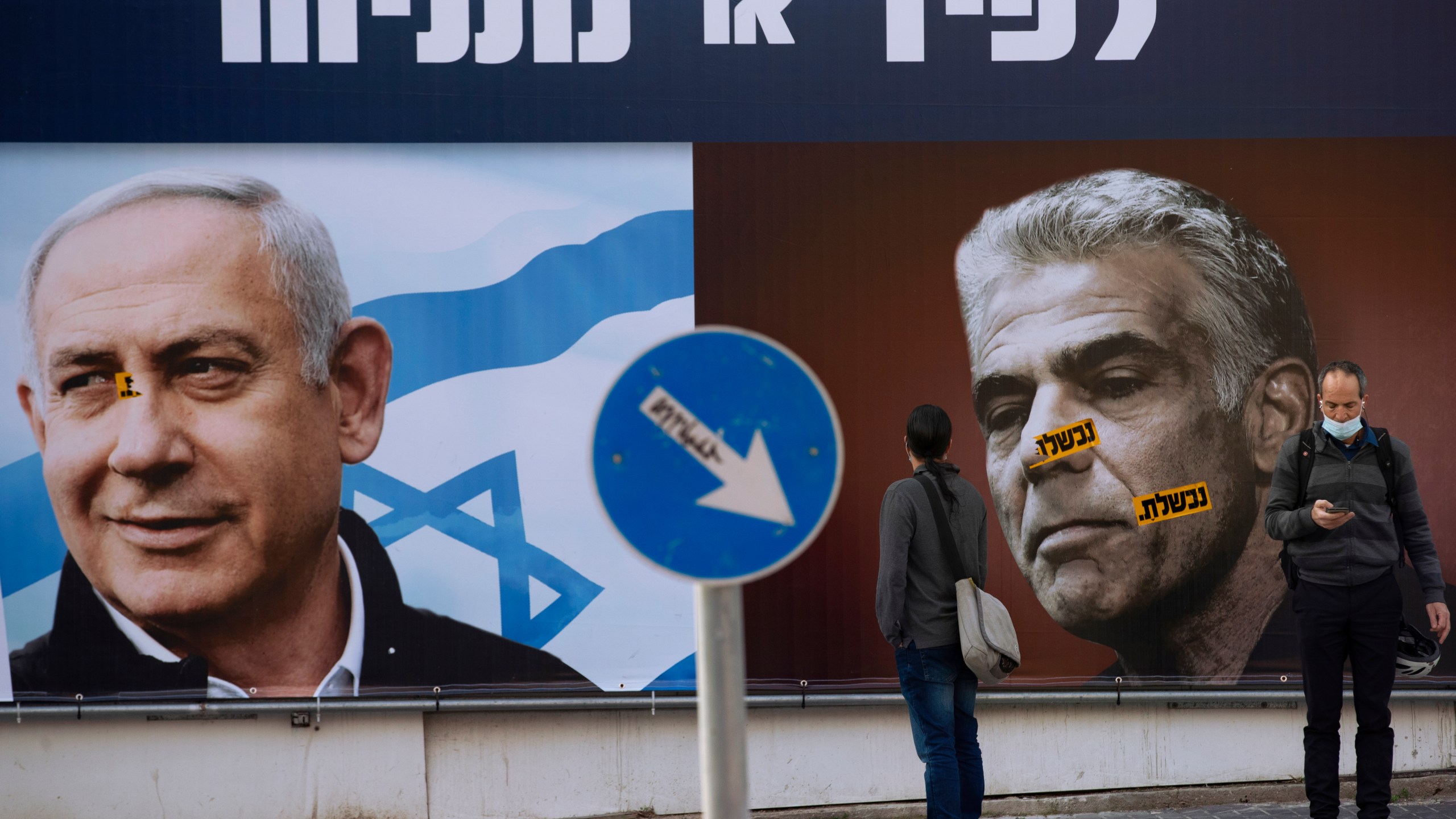 In this Sunday, March. 14, 2021 file photo, people stand in front of an election campaign billboard for the Likud party showing a portrait of its leader Prime Minister Benjamin Netanyahu, left, and opposition party leader Yair Lapid, in Ramat Gan, Israel. Israel's President Reuven Rivlin has tapped opposition leader Yair Lapid to form a new government, a step that could lead to the end of the lengthy rule of Prime Minister Benjamin Netanyahu. Rivlin announced his decision on live television a day after Netanyahu failed to cobble together a governing coalition by a midnight deadline. (AP Photo/Oded Balilty, File)