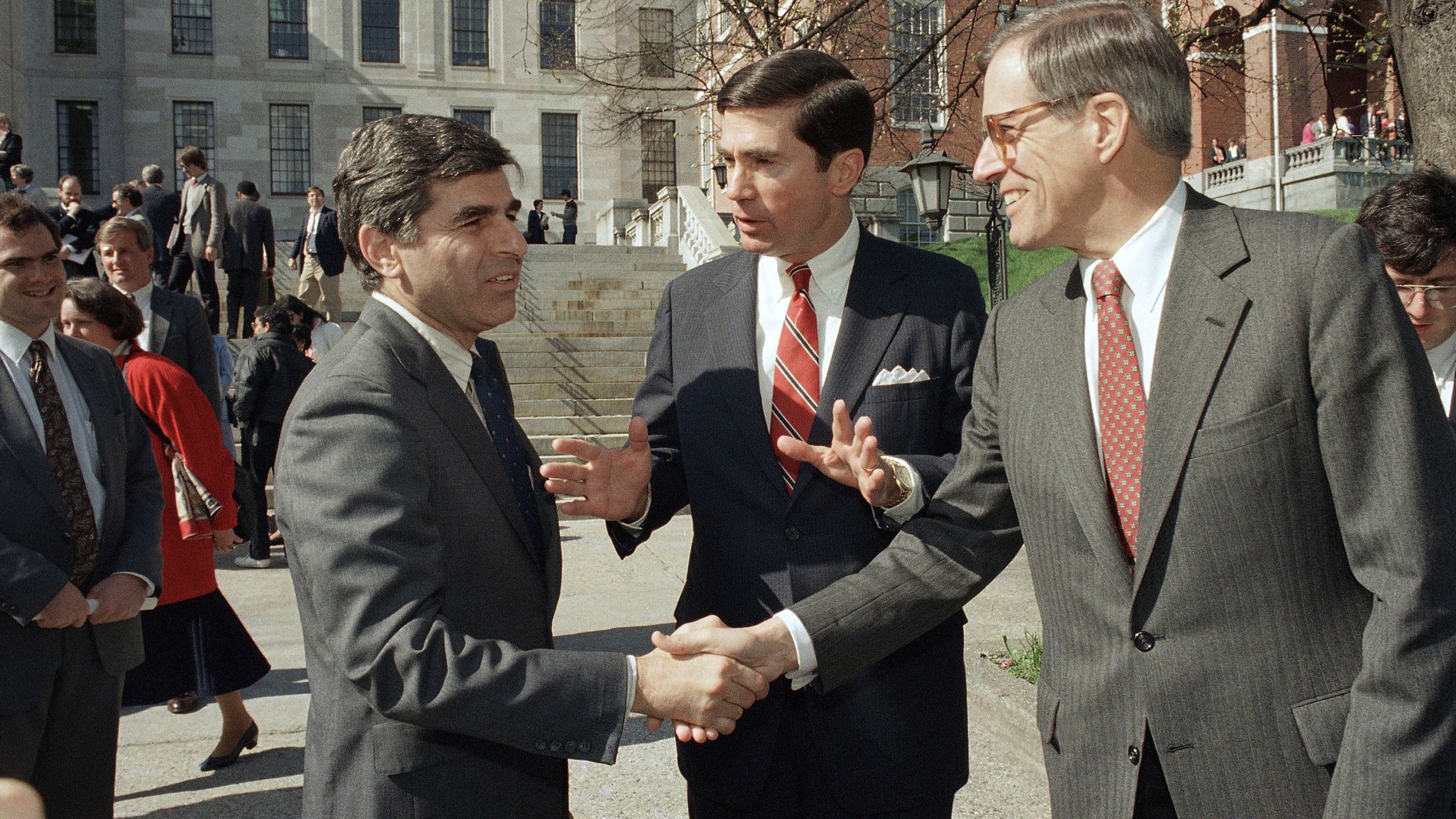 In this April 27, 1987, file photo, Massachusetts Governor Michael Dukakis, left, shakes the hands of former Delaware Governor Pierre Du Pont, right as former Virginia Governor Charles S. Robb looks on, after both men attended the Jobs for Bay State Grads program in Boston. (AP Photo/Jim Shea, File)