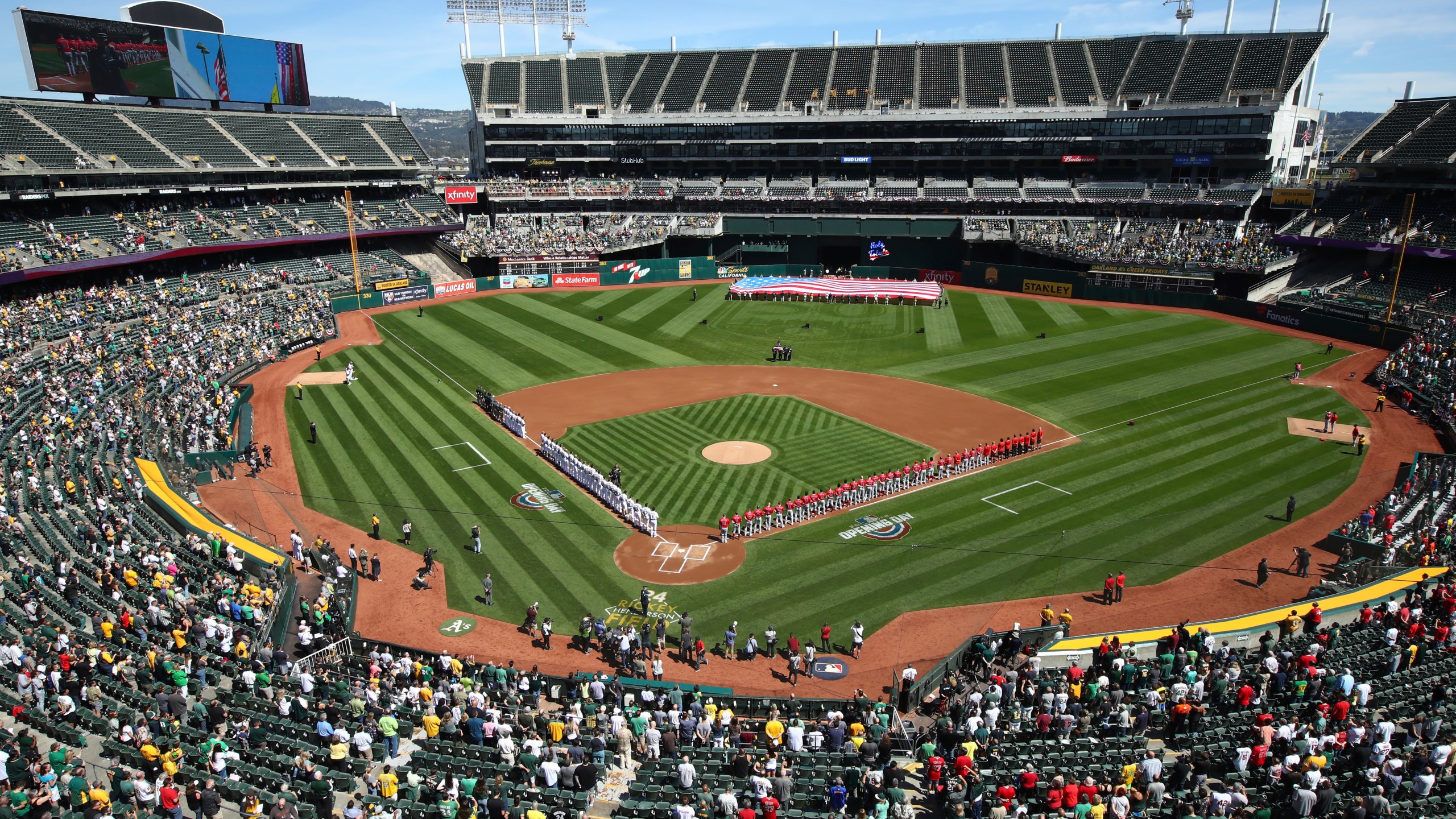 The Los Angeles Angels and Oakland Athletics stand for the national anthem at the Oakland Coliseum prior to an opening day baseball game in Oakland, Calif., in this Thursday, March 29, 2018, file photo.Major League Baseball instructed the Athletics to explore relocation options as the team tries to secure a new ballpark it hopes will keep the club in Oakland in the long term. MLB released a statement Tuesday, May 11, 2021, expressing its longtime concern that the current Coliseum site is “not a viable option for the future vision of baseball.” (AP Photo/Ben Margot, File)