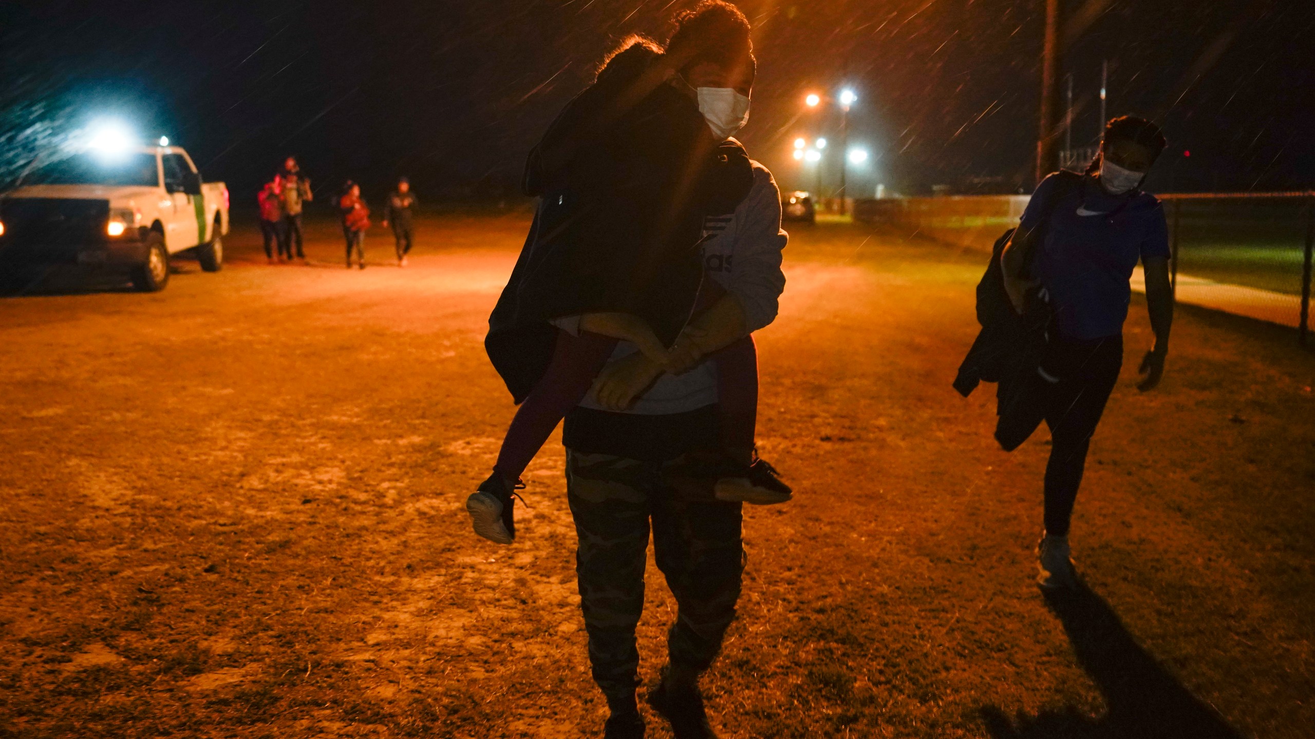 A migrant carries a child at an intake area after turning themselves in upon crossing the U.S.-Mexico border, late Tuesday, May 11, 2021, in La Joya, Texas. The U.S. government continues to report large numbers of migrants crossing the U.S.-Mexico border with an increase in adult crossers. But families and unaccompanied children are still arriving in dramatic numbers despite the weather changing in the Rio Grande Valley registering hotter days and nights. (AP Photo/Gregory Bull)