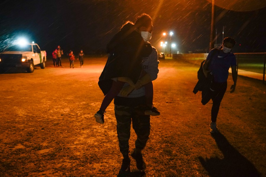 A migrant carries a child at an intake area after turning themselves in upon crossing the U.S.-Mexico border, late Tuesday, May 11, 2021, in La Joya, Texas. The U.S. government continues to report large numbers of migrants crossing the U.S.-Mexico border with an increase in adult crossers. But families and unaccompanied children are still arriving in dramatic numbers despite the weather changing in the Rio Grande Valley registering hotter days and nights. (AP Photo/Gregory Bull)