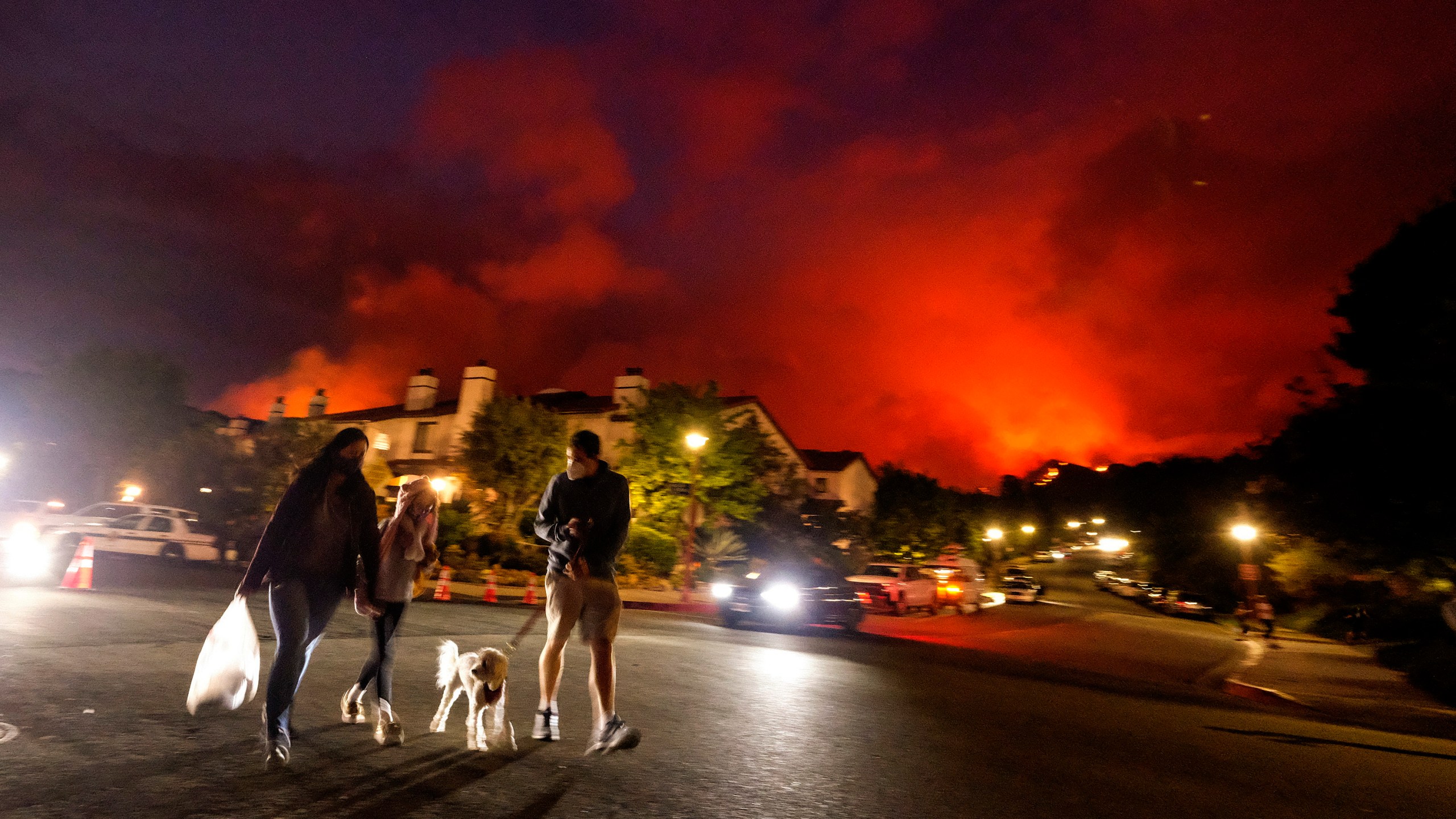 Residents walk a dog as a brush fire burns behind homes in the Pacific Palisades area of Los Angeles on Saturday, May 15, 2021. (AP Photo/Ringo H.W. Chiu)