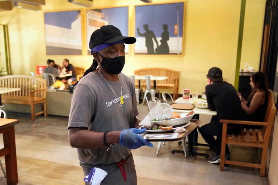 A worker in a face mask clears tables inside a covered patio in Burbank amid the COVID-19 pandemic on May 18, 2021. (Marcio Jose Sanchez / Associated Press)